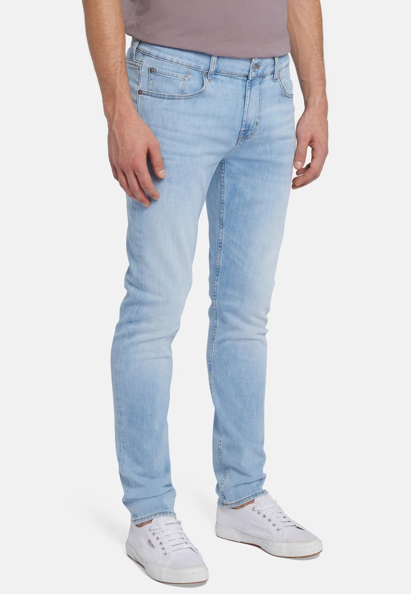 Jeans skinny azzurri in denim, con un classico design a cinque tasche e una leggera scoloritura. Abbinati a una maglietta grigia e sneakers bianche.