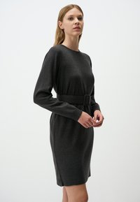 Robe en maille gris foncé avec des manches longues, un col rond et une taille ceinturée. Texture lisse, longueur genoux. Design simple sans motifs.