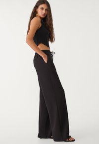Schwarzes, kurzes Tanktop mit Wellenkante, kombiniert mit locker sitzenden schwarzen Hosen mit einem elastischen Bund und Seitentaschen.