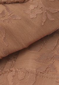 Gros plan sur un tissu brun avec un motif floral tricoté, présentant des formes de fleurs et de feuilles en relief et texturées.