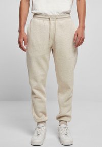 Beige sweatpants met een trekkoord in de taille, zijzakken en taps toelopende pijpen, gemaakt van zachte stof. Draagt met witte sneakers.