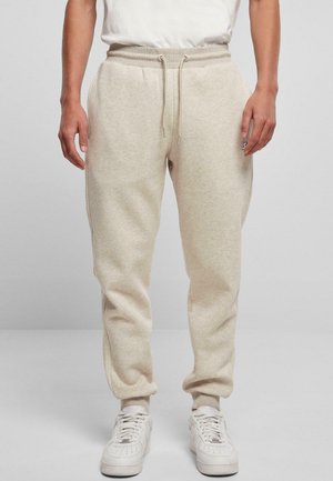 Beige sweatpants with a drawstring waist, side pockets, and tapered legs, made of soft fabric. Worn with white sneakers.
