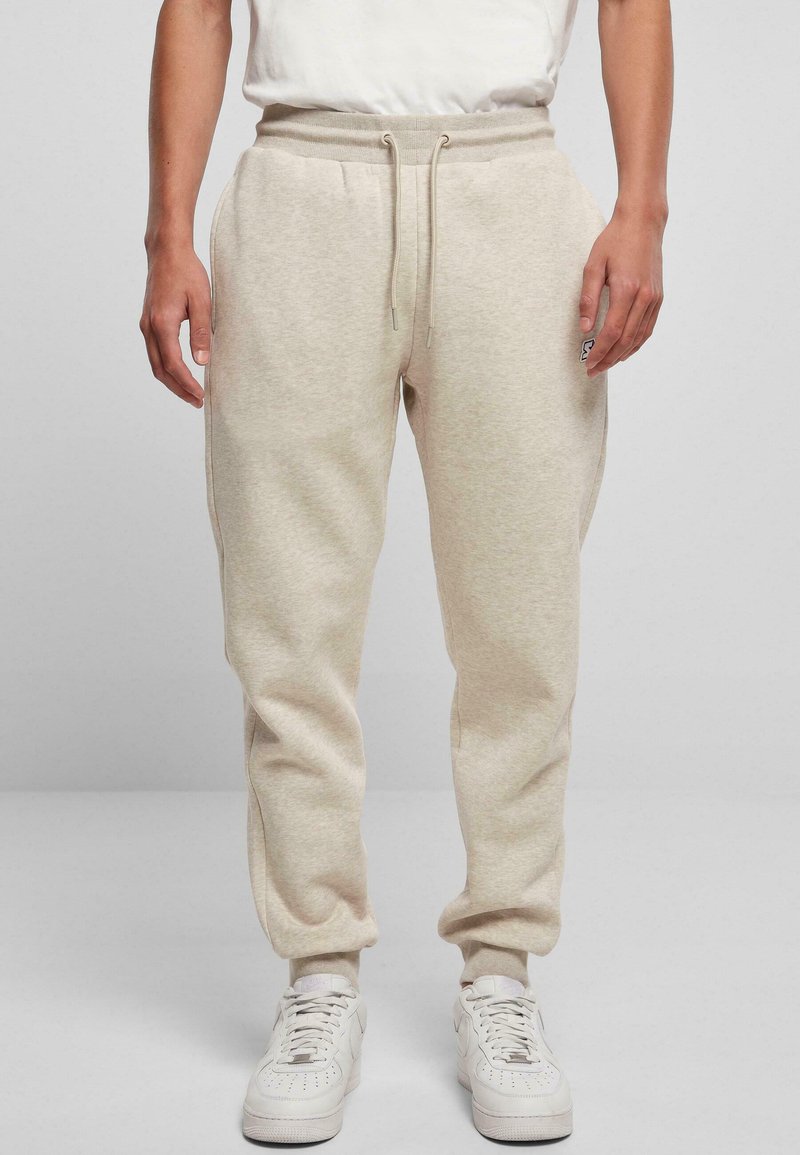 Beige sweatpants met een trekkoord in de taille, zijzakken en taps toelopende pijpen, gemaakt van zachte stof. Draagt met witte sneakers.