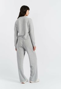 Maglione grigio a maglia e pantaloni larghi abbinati. Morbida texture, dettagli a coste sui polsini e sulla cintura. Modello mostrato di spalle.