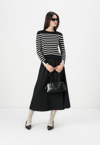 Haut à manches longues rayé noir et blanc, jupe noire, sac à main noir, chaussettes beiges et escarpins noirs à bout pointu. Texture lisse et design ajusté.