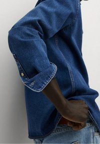 Denim overhemd met lange mouwen, blauwe kleur, opgerolde manchetten en contrasterende stiksels. Bevat een zijsplit-zoom en knoopdetails.