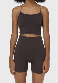 Top corto a coste marrone con spalline sottili abbinato a pantaloni corti marroni a vita alta. Entrambi i capi hanno una texture liscia e un design aderente.
