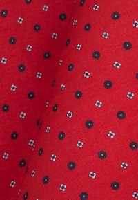 Czerwona tkanina z małymi, rozproszonymi wzorami kwiatowymi, z białymi kwiatami i granatowymi kółkami, tworzącymi teksturowany wzór.