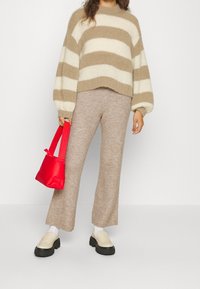 Pull rayé beige et crème avec manches ballons, associé à un pantalon en tricot beige et des mocassins à semelle épaisse noire. Tenant un sac à main rouge.