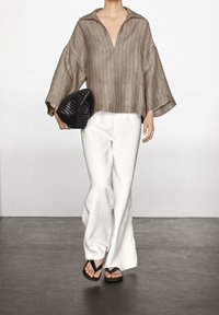 Brunstribet linned blouse med V-udskæring og brede ærmer, parret med hvide, lette bukser og sorte flip-flops. Accessory: sort vævet clutch.