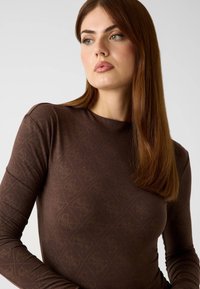 Bruine top met lange mouwen, voorzien van een getextureerd ruitpatroon en subtiele glans. Gemaakt van rekbare stof met een nauwsluitend silhouet.