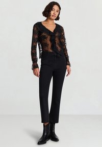 Camicia nera trasparente con dettagli in pizzo floreale, fronte arricciato e maniche lunghe, abbinata a jeans neri a vita alta e stivaletti.