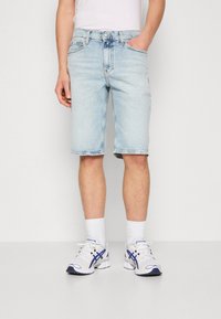 Shorts in denim azzurro con un fit classico e orlo grezzo. Abbinati a scarpe sportive bianche con accenti blu e calzini bianchi.