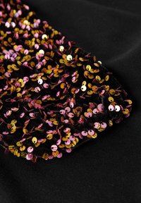 Tessuto nero con un gruppo di paillettes rosa e oro lucide, creando una superficie testurizzata con un mix di forme circolari e colori.