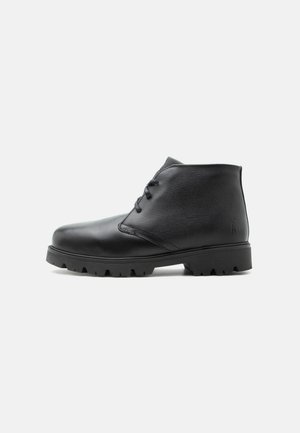 Bottine en cuir noir avec lacets à l'avant et semelle robuste, vue de profil sur un fond clair.
