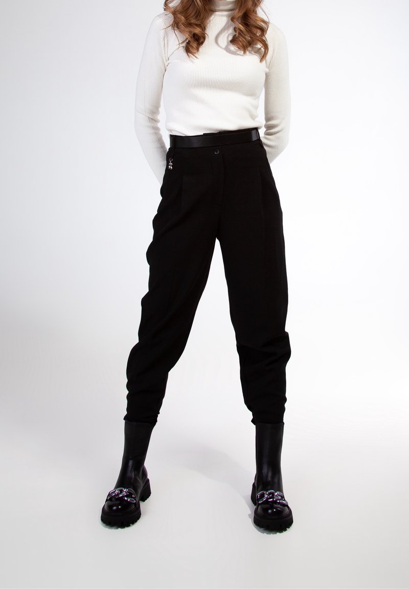 Pantalons noirs taille haute à coupe relaxed, avec des plis sur le devant. Associés à un col roulé en maille blanche et des bottines noires brillantes.
