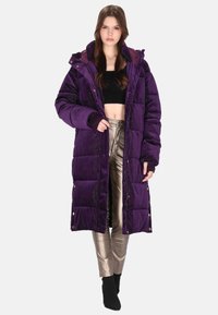 Fioletowa pikowana kurtka z kapturem, teksturowana tkanina, zatrzaski i luźny fason, noszona na czarnym krótkim topie i metalicznych srebrnych spodniach.