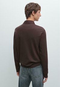 Bruine lange mouwen polo met een kraag, gemaakt van een zachte stof. Gecombineerd met lichtgrijze jeans met zichtbare achterzakken en naden.