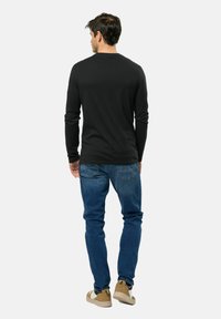 Chemise noire à manches longues avec un col rond, associée à un jean bleu et des chaussures de couleur claire, vue de dos.