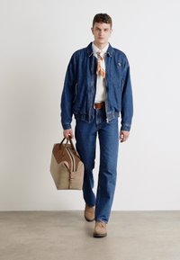 Veste en denim et jeans bleus, chemise blanche, et écharpe à motifs ; portant un sac souple marron avec une touche crème.