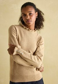 Beiger Pullover aus weichem Material. Mit geripptem Halsausschnitt und Bündchen sowie Knopfakzenten. Schlichtes Design mit lockerer Passform.