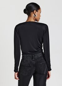 Langärmliges schwarzes Oberteil aus glattem Stoff, mit rundem Ausschnitt und gerafften Details, kombiniert mit hochgeschnittenen schwarzen Denim-Jeans.