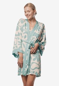 Jedwabny szlafrok w jasnym kremowym kolorze z dużymi turkusowymi abstrakcyjnymi wzorami, szerokimi rękawami, paskiem do zawiązania oraz luźnym krojem.
