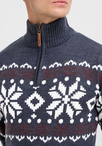 Gebreid marineblauw sweater met een kwart-rits kraag, gekenmerkt door een wit en bordeauxrood sneeuwvlokpatroon over de borst en geribbelde manchetten.