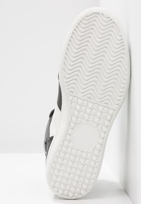 Černobílé tenisky s texturovanou gumovou podrážkou, disponující vzorovým gripem a zapuštěným kruhovým detailem na podrážce.