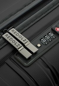 Close-up van een zwarte, gestructureerde kofferrits met twee metalen trekker en een combinatieslot met drie schakels ingesteld op 0-0-0.