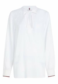 Blusa bianca con maniche lunghe, un collo rotondo e un dettaglio a fiocco sul davanti. Presenta polsini a contrasto con un accento di colore. Tessuto morbido.