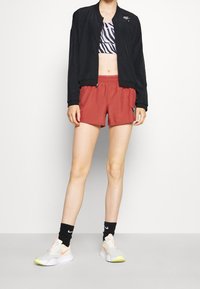 Mustat bomber-takki, seepra-kuosiset crop-top, punaiset shortsit ja valkoiset lenkkarit neon-aksentilla, yhdistettynä mustiin nilkkasukkahousuihin.