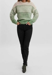 Vihreä ja kerma-valkoinen raidallinen neulepaita, jossa on pyöreä kaula-aukko ja ribbireunus, yhdistetty mustiin kapeneviin housuihin ja tumman vihreisiin nilkkabootseihin.