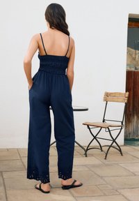 Mono ligero azul marino con corpiño fruncido, tirantes ajustables y ribete de encaje en el dobladillo. Se lleva con chanclas negras.