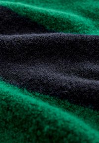 Tissu en laine affichant des sections vert foncé et noires, avec une surface douce et texturée, légèrement brillante et d'épaisseurs variées.