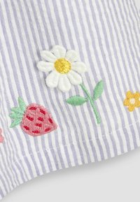 Tissu brodé mettant en valeur des marguerites blanches, des fraises roses et des fleurs colorées sur un matériau rayé bleu clair et blanc. Fini texturé.