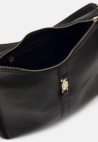 Bolso de mano de cuero negro con cierre superior, herrajes dorados y un bolsillo interior con forro estampado. Detalles de textura y diseño notables.