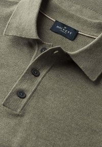 Polo en maille taupe avec col, trois boutons noirs, et étiquette noire "Hackett London" cousue à l'intérieur du col.