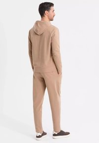 Beige hoodie och sweatpants-set gjort av mjukt material, med en känguruficka, ribbade ärmslut och en avslappnad passform. Bruna sneakers fulländar looken.