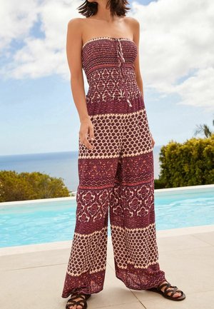 Combinaison bustier avec un corsage ajusté, jambes larges, et un motif contrastant bordeaux et beige. Le tissu est léger et texturé.