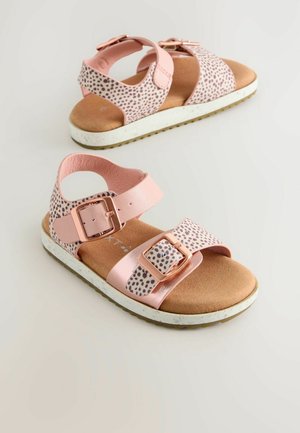 Sandales roses avec des lanières à pois, dotées d'une fermeture à boucle, d'une semelle intérieure douce et d'une semelle blanche texturée avec des accents éparpillés.