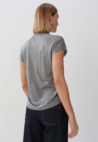 T-shirt grigio a maniche corte realizzato in tessuto morbido, con scollatura rotonda e maniche leggermente arrotolate, abbinato a jeans scuri.