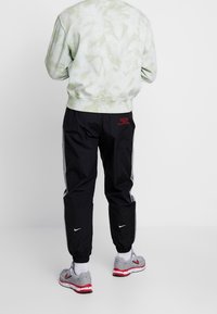 Pantalons de sport noirs avec des bandes latérales, des poignets élastiques et des détails en texte rouge ; associés à un sweat-shirt tie-dye vert clair et des baskets grises.