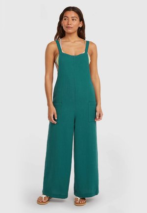 Combinaison en coton bleu sarcelle à jambes larges, avec deux poches avant et bretelles ajustables. Le tissu texturé apporte de la profondeur au design.