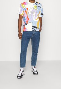 Grafisk bomullströja med flerfärgade abstrakta mönster och texten "Love Unite" tillsammans med Adidas-logotypen. Kombinerad med blå jeans och sneakers.