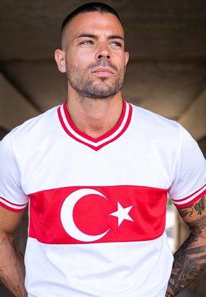 Witte T-shirt met rode horizontale streep, versierd met een halve maan en ster. V-hals ontwerp met rode accenten op de mouwen. Soepele stofstructuur.