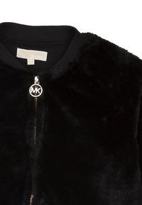 Černá bunda z umělé kožešiny s žebrovaným límcem a viditelným zlatým jezdcem na zipu s logem "MK", štítek Michael Kors uvnitř límce.