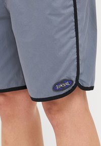 Costume da bagno grigio con rifiniture nere, con orlo arrotondato e un'etichetta logo blu, bianca e nera sulla gamba inferiore. Tessuto liscio.