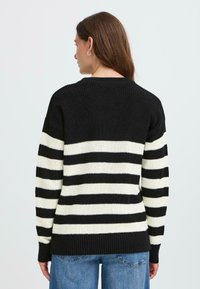 Svart og hvitstripet genser, ribbet tekstur, lange ermer, rund hals, kontrasterende horisontale striper, vist fra baksiden.