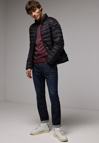 Mustat puffatakki, jossa on tilkkupaketti, marooni villapaita alla, siniset farkut ja valkoiset lenkkarit vaaleilla yksityiskohdilla.